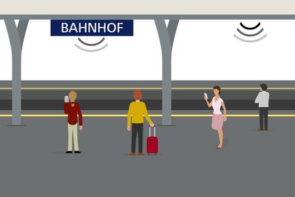 Das Bild zeigt einen Bahnsteig mit Bahnsteigdach und Menschen, die das Service WLAN am Bahnhof nutzen. 