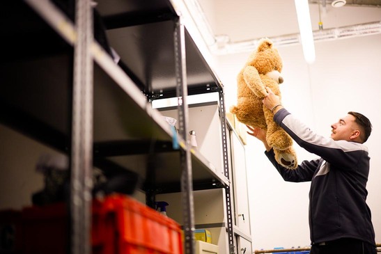 Ein Lost and Found Mitarbeiter hebt einen übergroßen Teddybären in ein Regal.