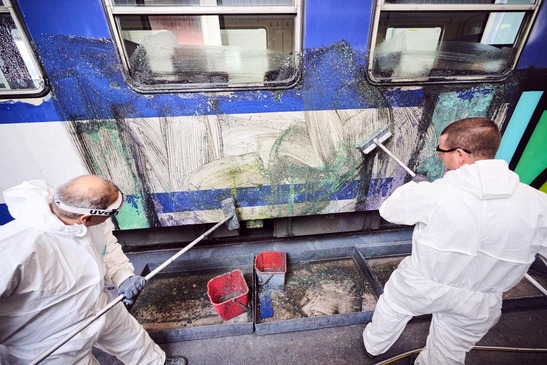 Two employees clean graffiti off a train
