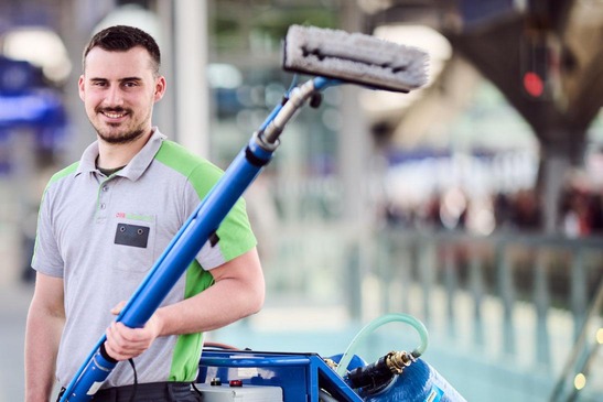 Reinigungsmitarbeiter mit einem Teleskopwischer in der Hand.