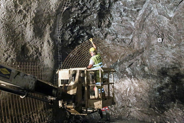 A miner attaches several steel grids to the rock face.