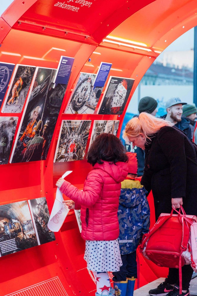 Two children marvel at the displayed pictures. The pictures are about the tunnel construction.