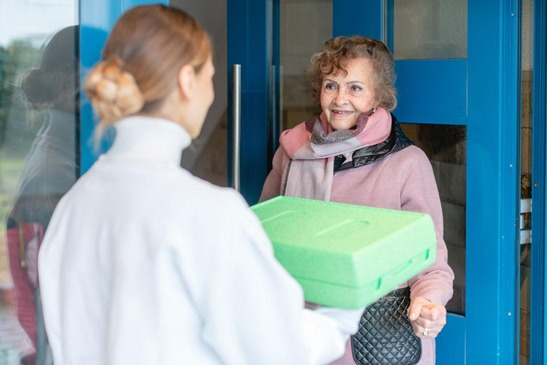 Pensionistin nimmt Essenslieferung entgegen.
