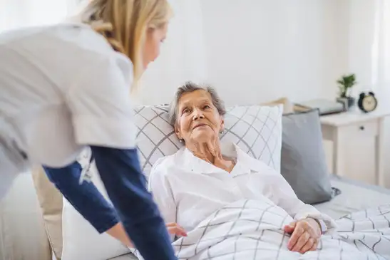 Kranke Frau muss gepflegt werden und liegt im Bett.