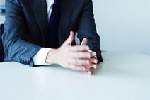 Business-Mann am Schreibtisch, der redet. Man sieht nicht seinen Kopf, nur den Oberkörper und die Hände stehen im Mittelpunkt.