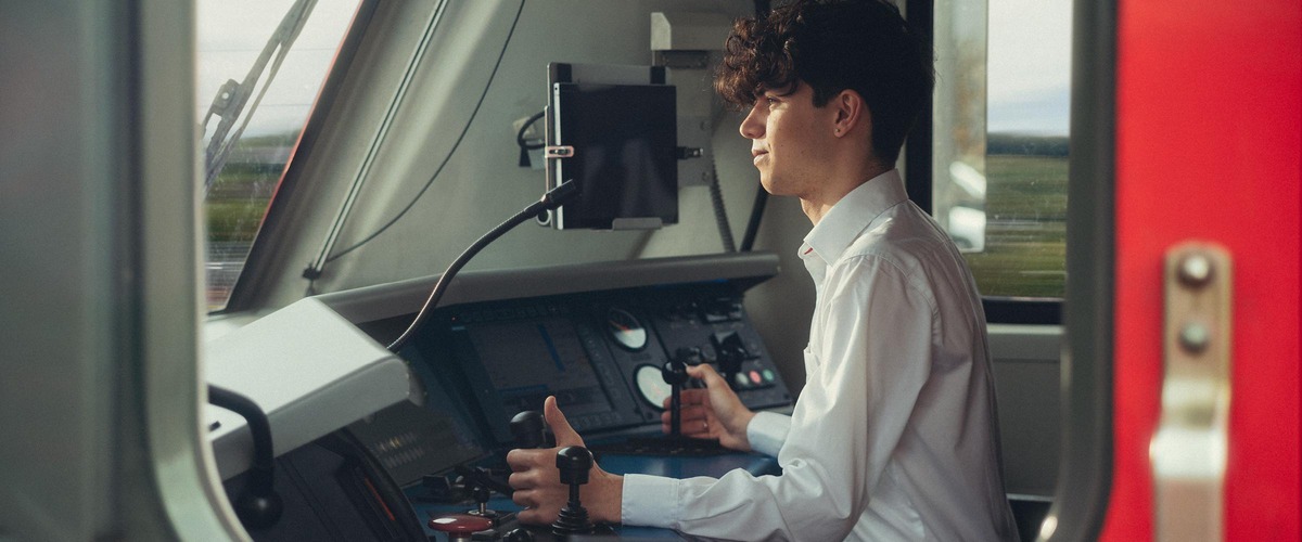 Mann in einer Lok sitzend, mit weißen Hemd und dunkelbraunen Haaren.