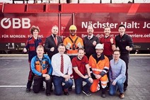 Eine Mitarbeitergruppe mit unterschiedlichen Uniformen, vor einer roten Lok stehend.