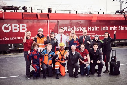 Eine Gruppe Mitarbeitende der ÖBB in verschiedenen Uniformen jubelnd und vor einem Zug stehend