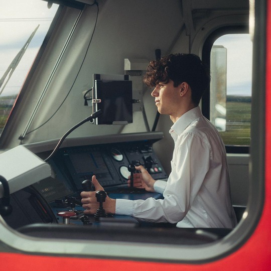 Mann in einer Lok sitzend, mit weißen Hemd und dunkelbraunen Haaren.