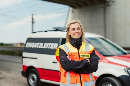 Junge Frau mit Warnweste und blonden Haaren. Stehend mit verschränkten Armen vor einem Einsatzfahrzeug