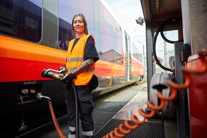 Junge Frau mit orangener Warnweste stehend vor einem Zug 