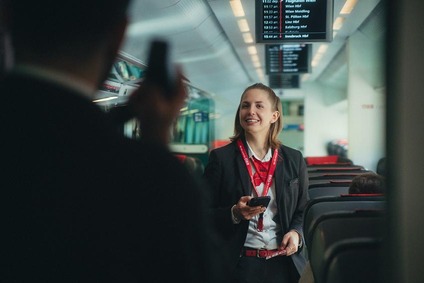 Eine weibliche Zugbegleiterin in einen Zug stehend, mit ÖBB Uniform lächelnd. 
