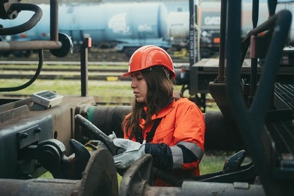 Frau in orangener Uniform, zwischen zwei Zügen stehend am verkuppeln.