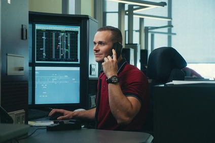 Mann in roten T-Shirt vor Bildschirmen am Telefon.