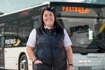 Frau in weißen Hand und schwarzen Gilet. Steht vor einem Postbus