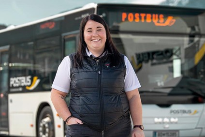 Frau in weißen Hand und schwarzen Gilet. Steht vor einem Postbus
