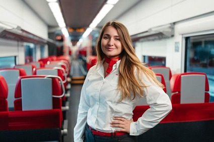 junge Frau mit blond-braunen Haaren und weißer Bluse. Stehend in einem Zug