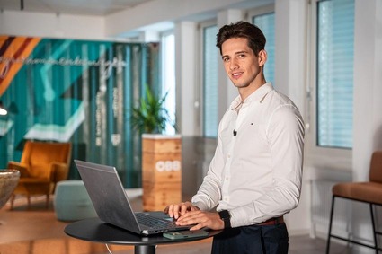 Junger Mann mit weißen Hemd und dunklen Haaren. Stehend mit Laptop