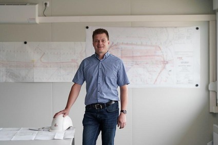 Mann mit kurzen Haaren und kariertem Hemd steht vor einem Bauplan.