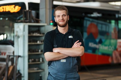 Mann mit kurzen braunen Haaren vor einem Bus stehend mit Werkzeug