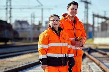 Zwei Mitarbeitende in orangener Uniform stehen im Gleisbereich.