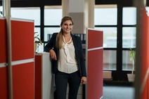 Junge Frau stehend angelehnt mit braunen langen Haaren und in die Kamera lächelnd