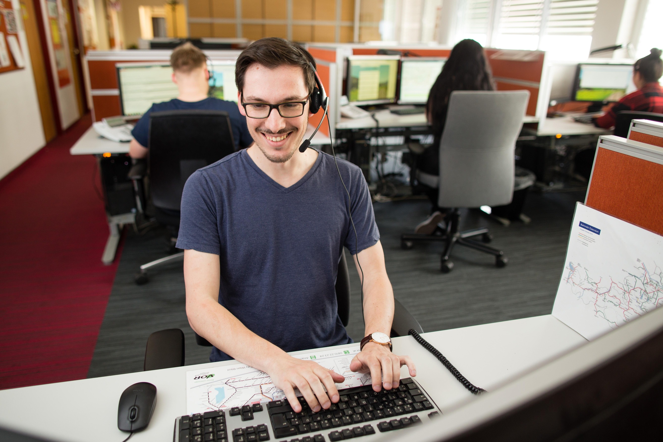 Mann mit Brille und T-Shirt am Computer sitzend.