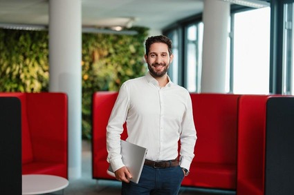 Mann mit weißen Hemd und kurzen Haaren im Arm einen Laptop haltend.