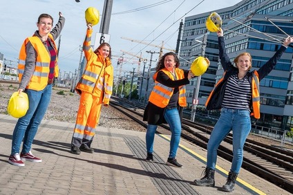 Menschengruppe mit Warnweste und gelben Schutzhelmen jubelnd. 