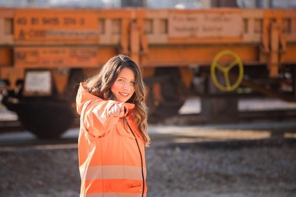 Eine Frau mit braunen Haaren und orangener Uniform zeigt in die Kamera. 