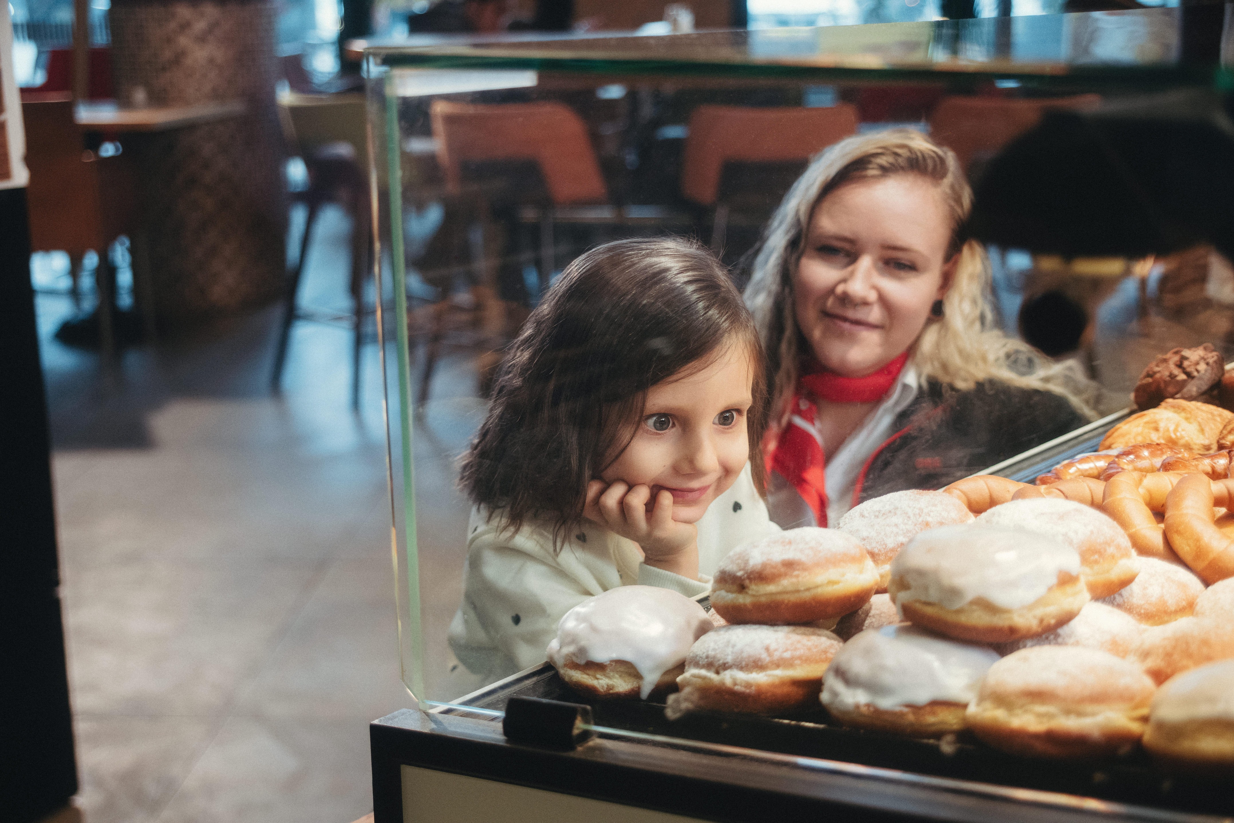 ÖBB MItarbeiterin mit Kind. Kind schaut erfreut auf die Vitrine eines Bäckers<br/>