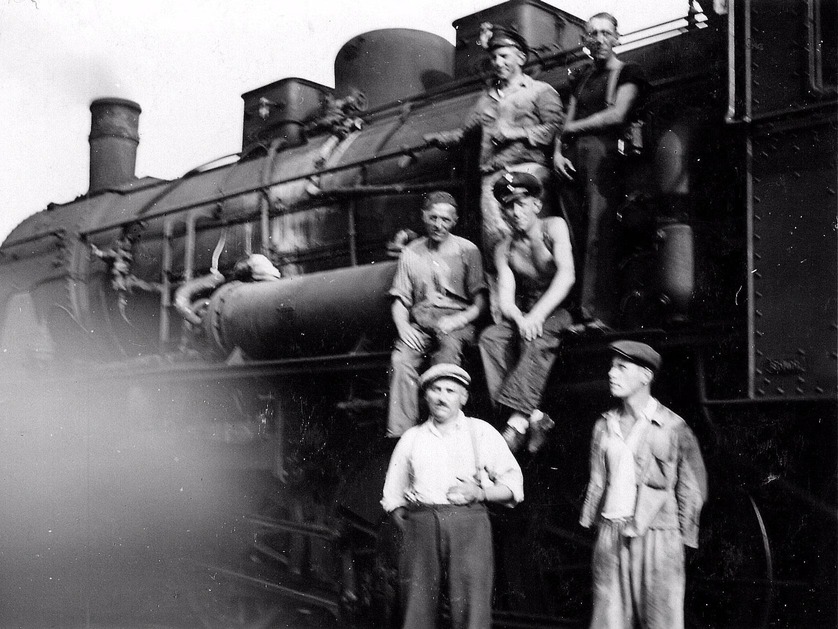 Eisenbahner stehen vor und sitzen auf Lokomotive