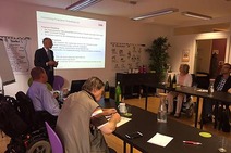 Sitzende Personen, die dem Moderator zuhören, der zum Ticketshop 2.0 erzählt