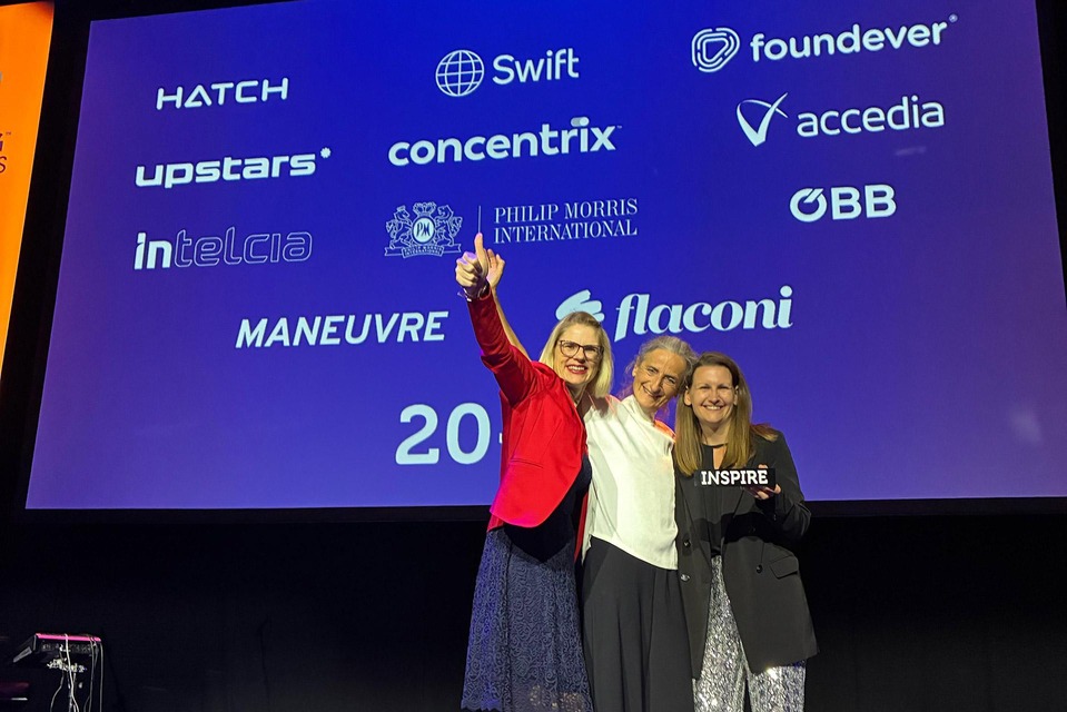 Drei ÖBB Mitarbeiterinnen stehen auf der Bühne und lachen in die Kamera. Eine Kollegin hält den Inspiring Workplace Award (ein schwarzer Quader auf dem in weißer Schrift „Inspire“ steht) in der Hand.
