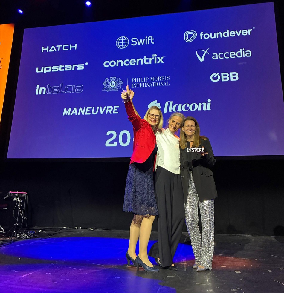 Drei ÖBB Mitarbeiterinnen stehen auf der Bühne und lachen in die Kamera. Eine Kollegin hält den Inspiring Workplace Award (ein schwarzer Quader auf dem in weißer Schrift „Inspire“ steht) in der Hand.