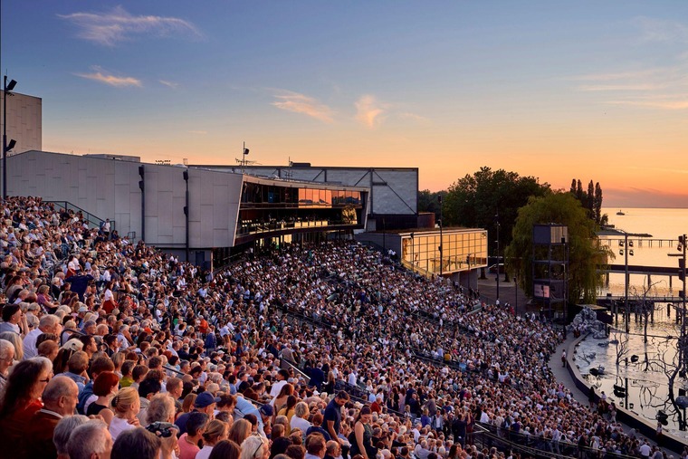 Bregenz Sehenswürdigkeiten: Blick über das Publikum bei einer Aufführung der Bregenzer Festspiele. Im Hintergrund der See und ein abendlicher Himmel. 
