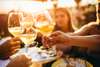 Essen in Wien: Blick auf einen Tisch mit Freunden, die mit einem Glas Wein anstoßen. Die Sonne steht im Hintergrund. 
