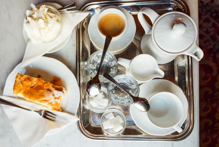 Essen in Wien: Blick von oben auf einen Tisch im Kaffeehaus mit klassischem Kaffeehaus-Gedeck. Kaffeetassen, Kaffeekanne, ein gefülltes Wasserglas, Apfelstrudel und Schlagobers. 