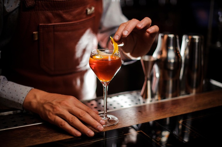 Essen in Wien: Man sieht den Tresen einer Cocktailbar, auf der ein Bartender ein Minzblättchen im Cocktail zurechtrückt. 