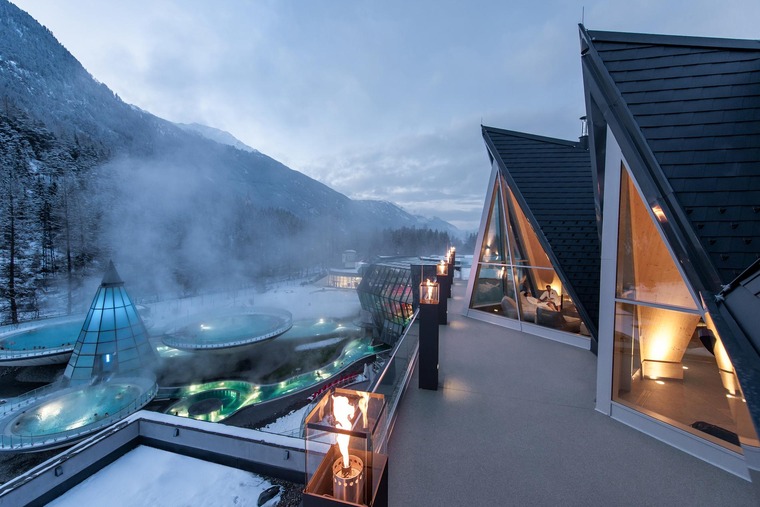 Wellness in Österreich: Blick auf den Außenbereich der Aqua Dome Therme in Tirol. Die Pools dampfen in der kalten Winterluft. 