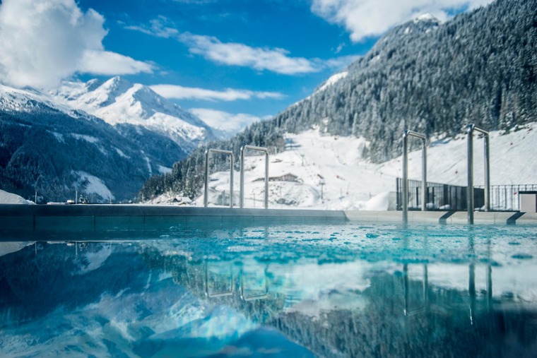 Wellness in Österreich: Blick auf den Außenpool der Felsentherme in Bad Gastein, dahinter schneebdeckte Gipfel. 