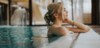 Wellness in Österreich: Eine Frau steht am Beckenrand und hat die Augen genüsslich geschlossen, hinter ihr hellblaues Wasser. 