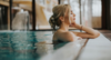 Wellness in Österreich: Eine Frau steht am Beckenrand und hat die Augen genüsslich geschlossen, hinter ihr hellblaues Wasser. 