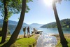 Österreich See Urlaub: Blick auf den Millstätter See. Zwei Wanderer stehen neben einem kleinen Steg mit einer Bank, und blicken auf den See. 