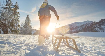 Eine Person zieht in einer schneebedeckten Landschaft einen Schlitten hinter sich her