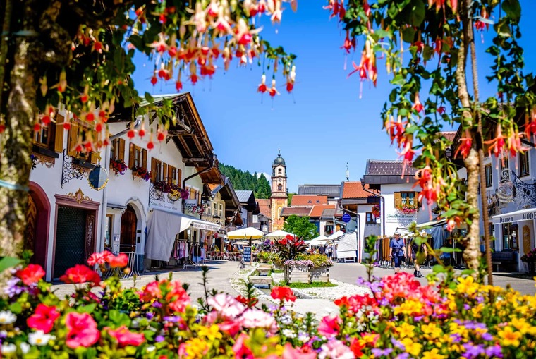 Tirol Ausflugsziele, aber in Bayern: Auf dem Bild sieht man bemalte Häuser in Mittenwald, im Vordergrund bunte Blumen. 