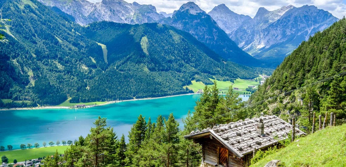 Tirol Ausflugsziele: Blick auf den Achensee in Tirol und die dahinterliegenden Berge. Im Vordergrund eine Almhütte. 