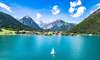Tirol Ausflusgsziele: Auf dem Bild sieht man den türkisfarbenen Achsensee im Sommer. Auf dem ganzen See ist nur ein Segelboot zu sehen, im Hintergrund die Berge. 