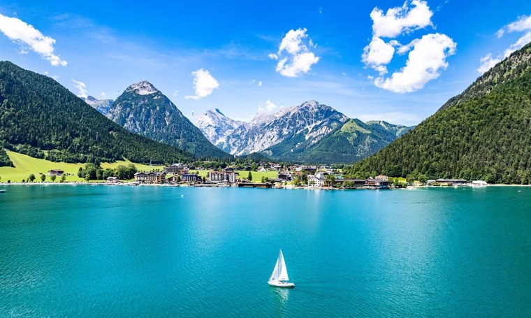 Tirol Ausflusgsziele: Auf dem Bild sieht man den türkisfarbenen Achsensee im Sommer. Auf dem ganzen See ist nur ein Segelboot zu sehen, im Hintergrund die Berge. 