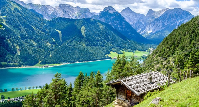 Tirol Ausflugsziele: Blick auf den Tiroler Achensee mit den Bergen im Hintergrund. Im Vordergrund eine Almhütte. 
